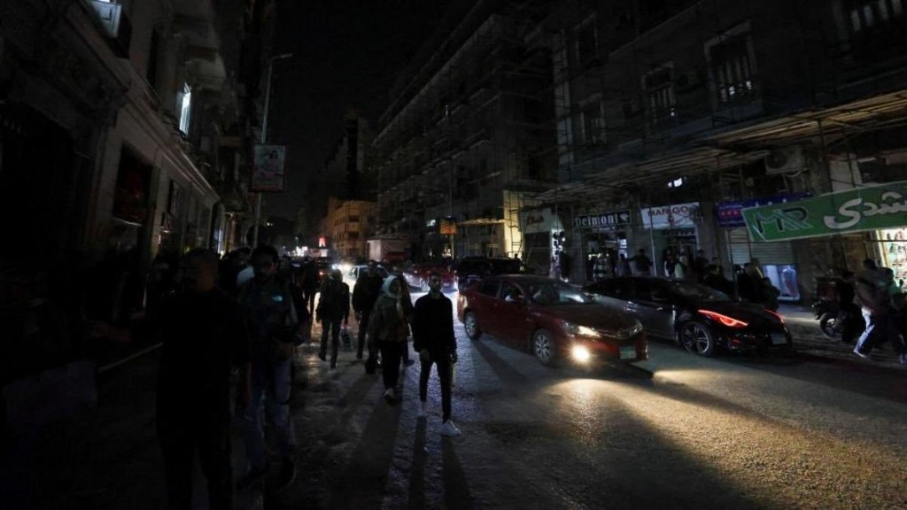 Night street in Egypt: darkened road, pedestrians and cars, headlights cutting through blackout conditions